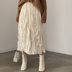 Person wearing a beige pleated skirt and white boots against a plain background