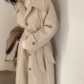 Beige trench coat worn by a person against a neutral background
