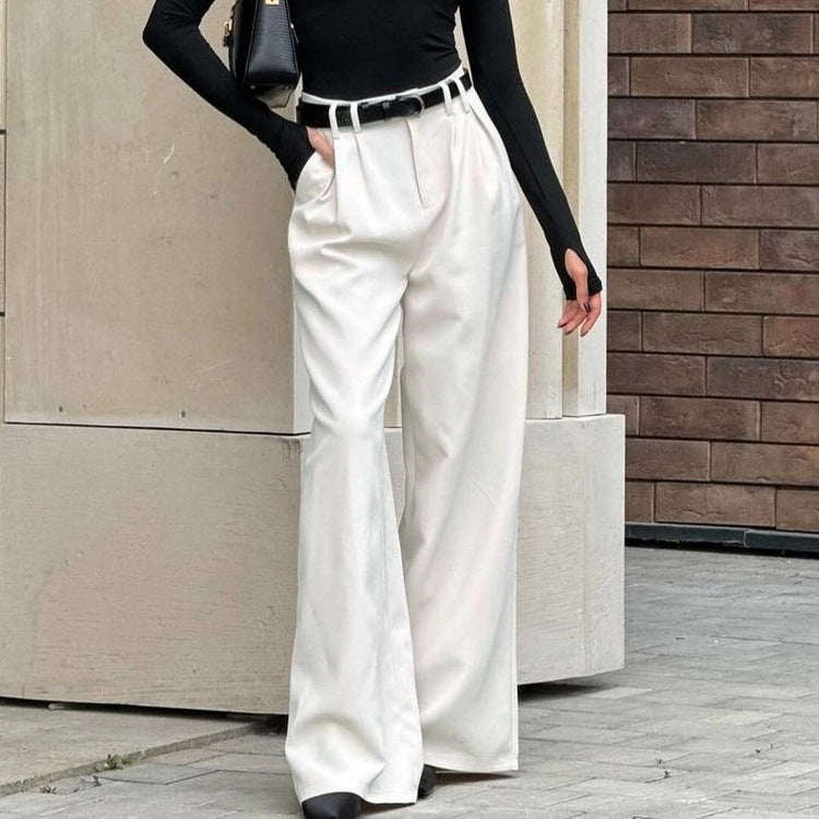 Person wearing white wide-leg pants and a black top against a wooden wall.