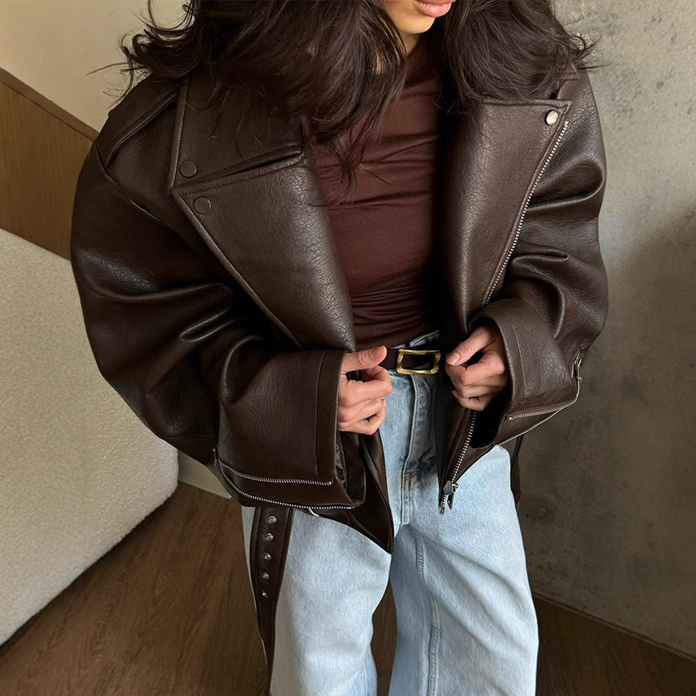 Person wearing a brown leather jacket and light blue jeans indoors.